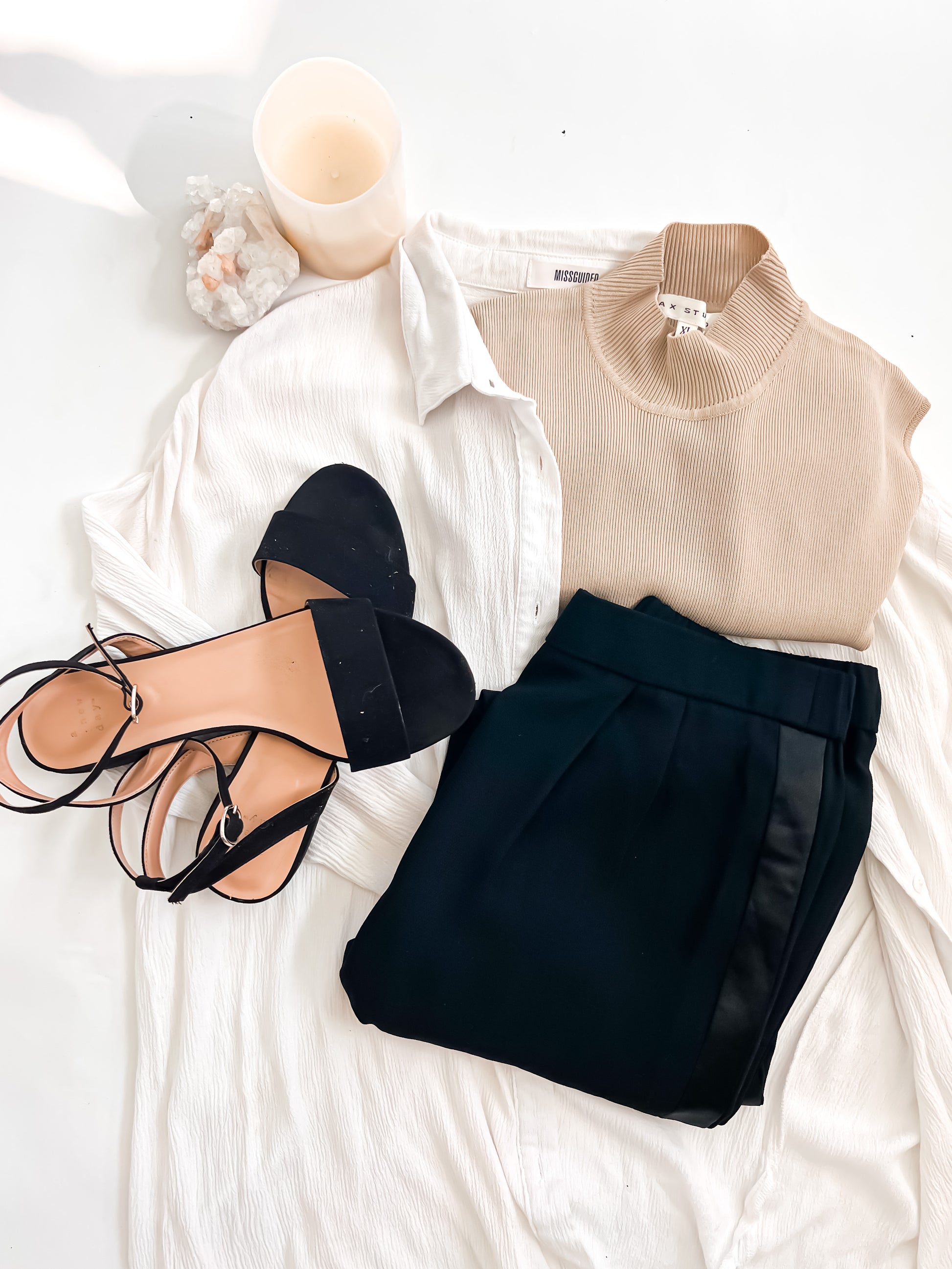 Fashionable outfit with beige top, black shorts, and sandals on a white surface.